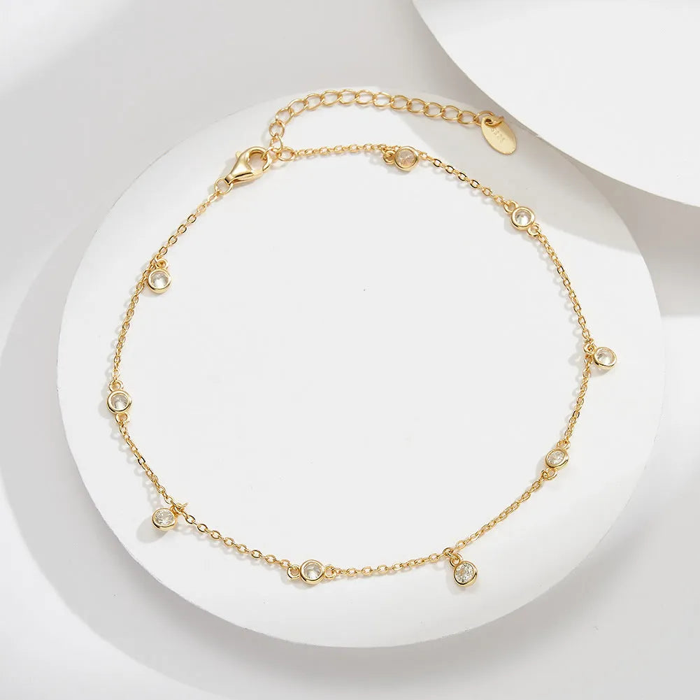 Close-up of a women's silver anklet with a geometric zirconium pendant on a simple chain.