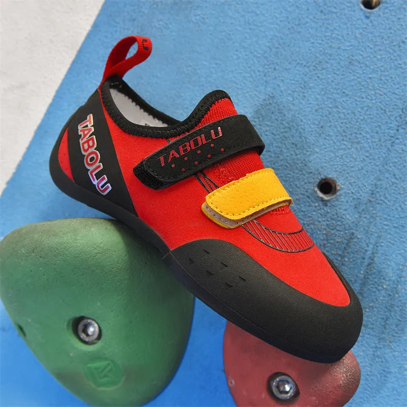 Black and red beginner rock climbing shoes with velcro strap and rubber sole on a climbing hold.