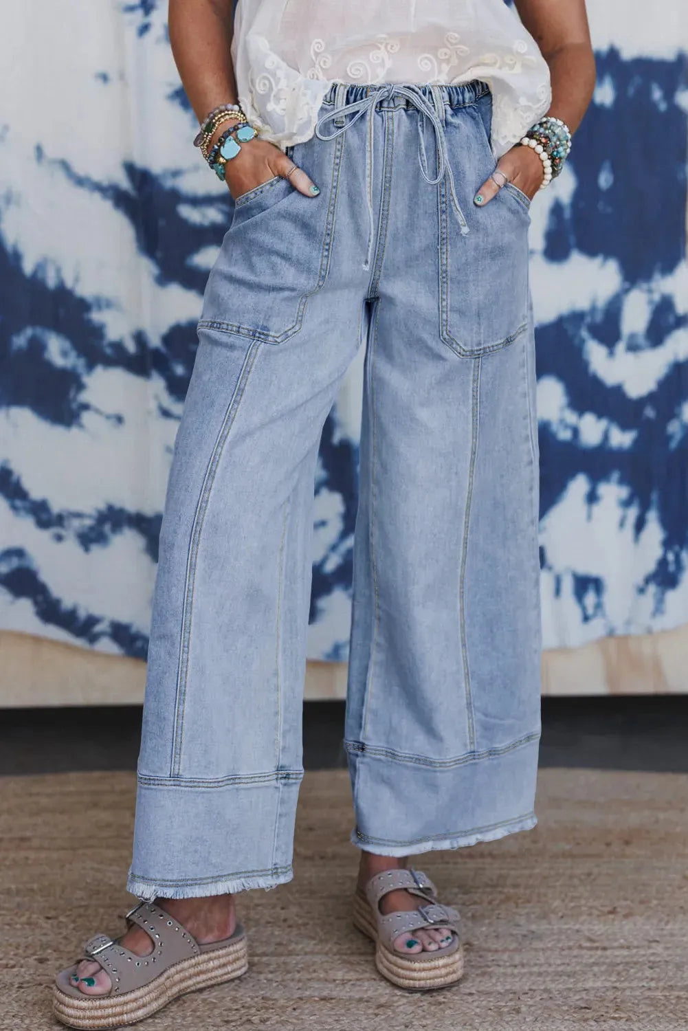 Beau blue wide-leg women's denim trousers with an elasticated drawstring waist and raw hem seam detail laid flat.