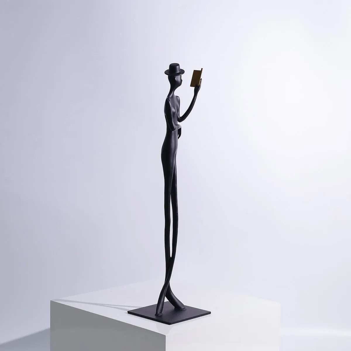 Black cast aluminium sculpture of a woman reading, modern minimalist desk decor.