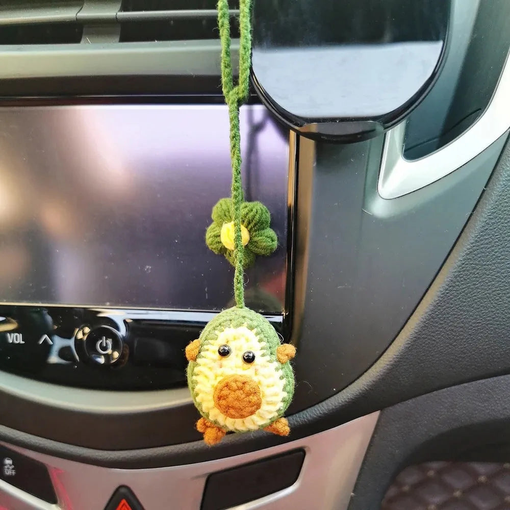 Handmade crocheted avocado-shaped car pendant with a rainbow flower on a green background.