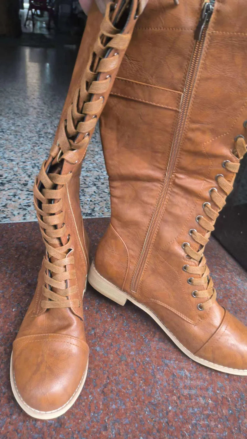 Women's black artificial PU knight boots with cross-strap and buckle fastening.