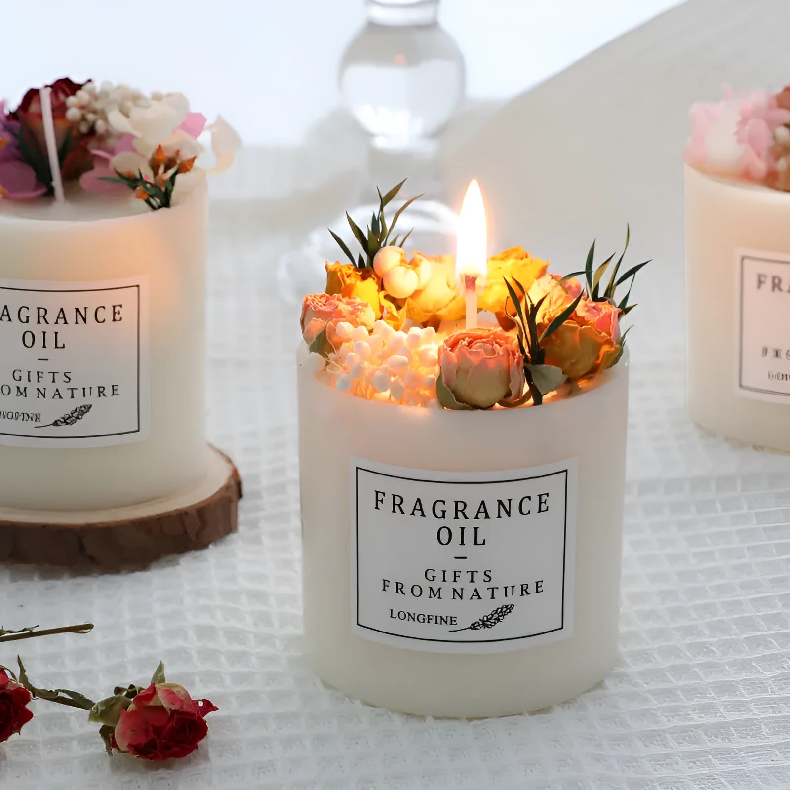 Decorative scented candle with dried flowers inside, shown with wooden chip base and gift box packaging.