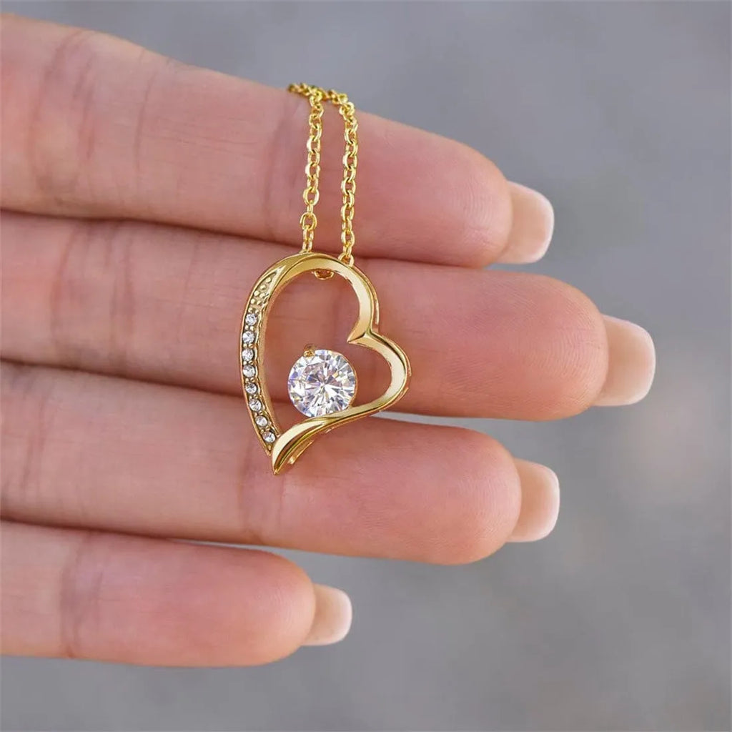 Silver and gold hollow heart necklace pendant presented on a card inside an open gift box.