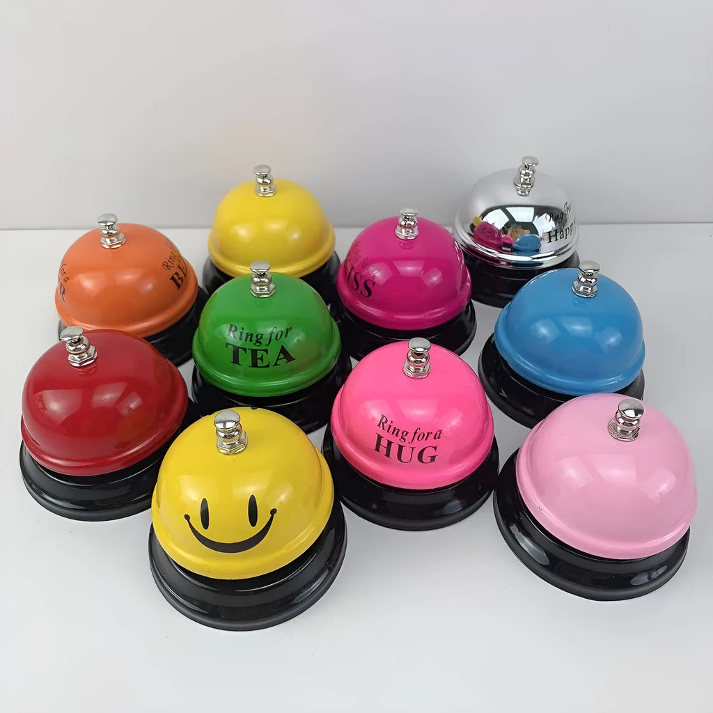 Iron table serving bell in multiple colour options on a wooden surface.