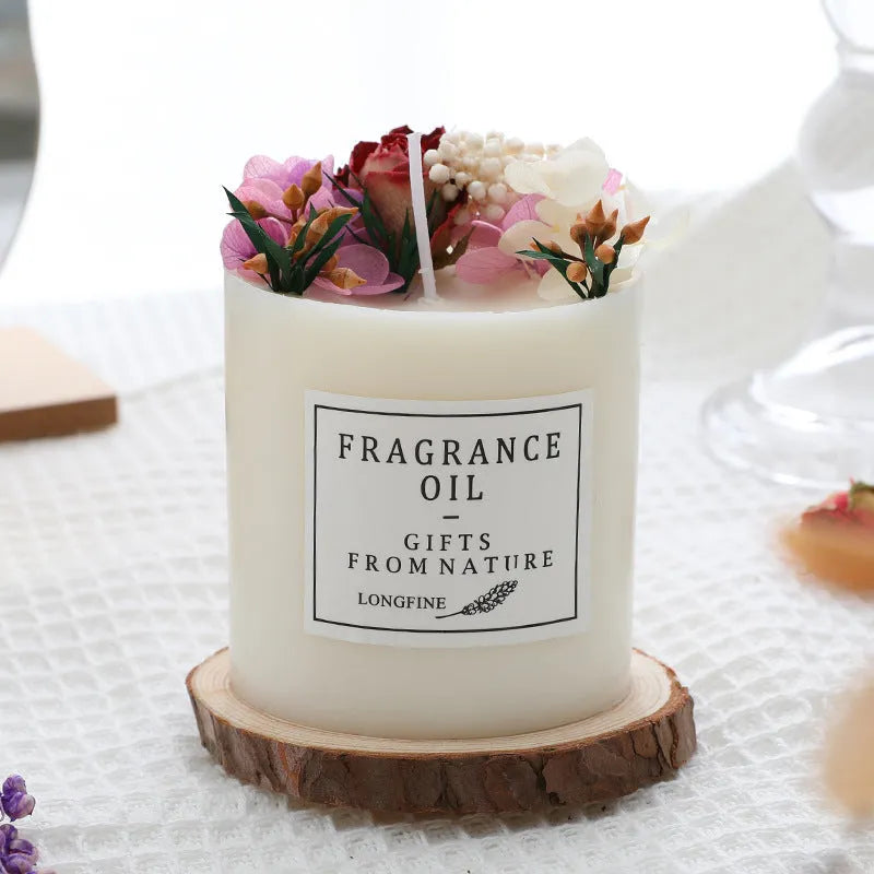 Decorative scented candle with dried flowers inside, shown with wooden chip base and gift box packaging.