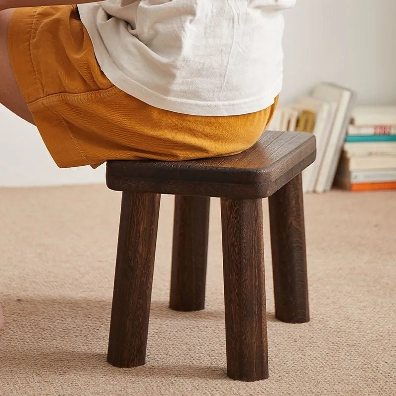 Solid wooden shoe changing stool with a distressed finish, shown in a living room setting.