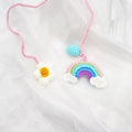 Handmade crocheted avocado-shaped car pendant with a rainbow flower on a green background.