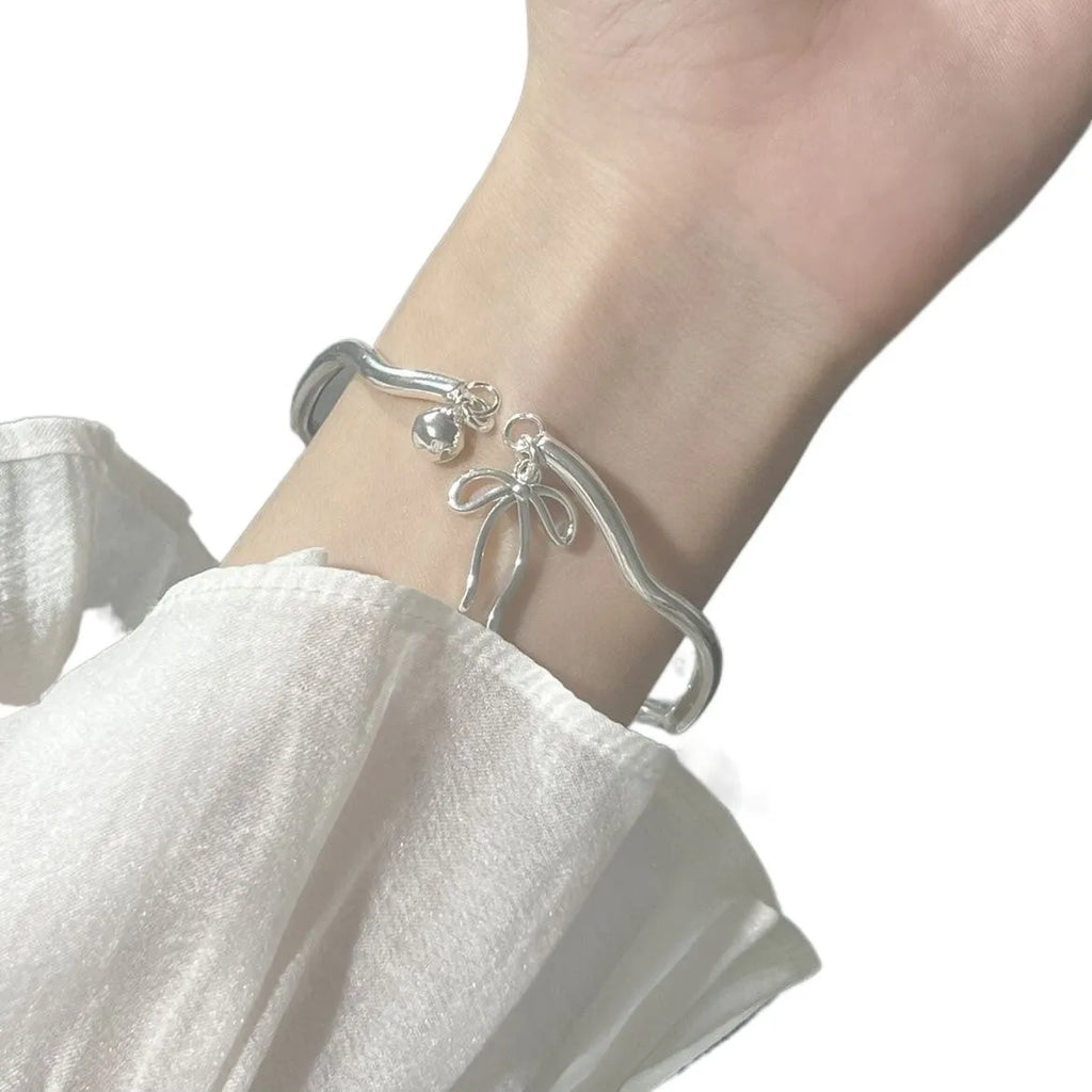 Silver adjustable bracelet with bow detail and bell opening clasp on wrist