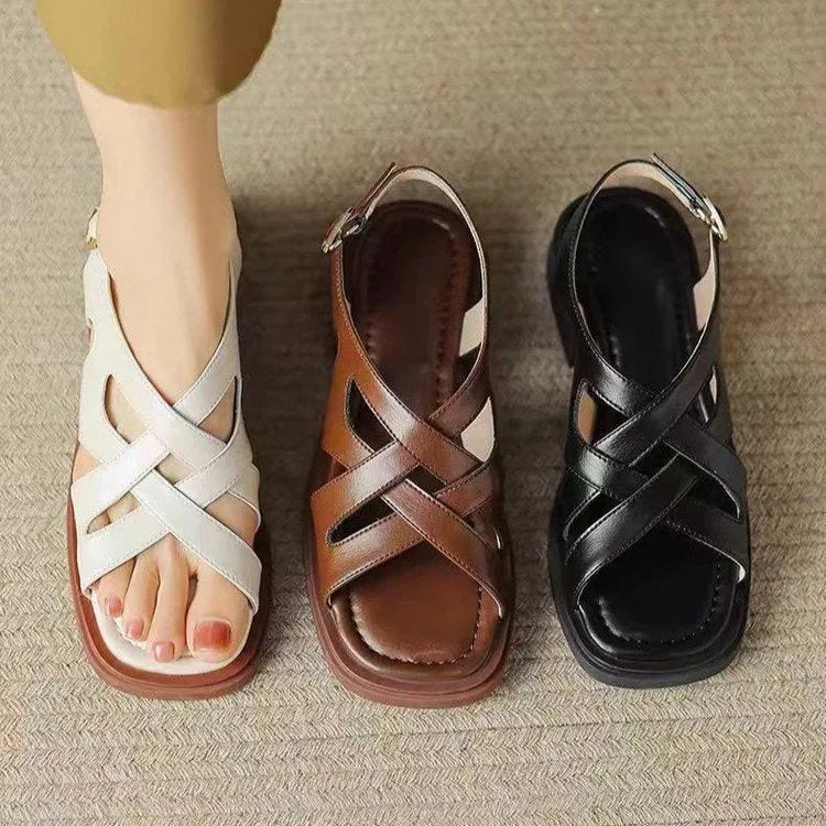 Women's black patent leather square toe sandals with cross strap on a white background.