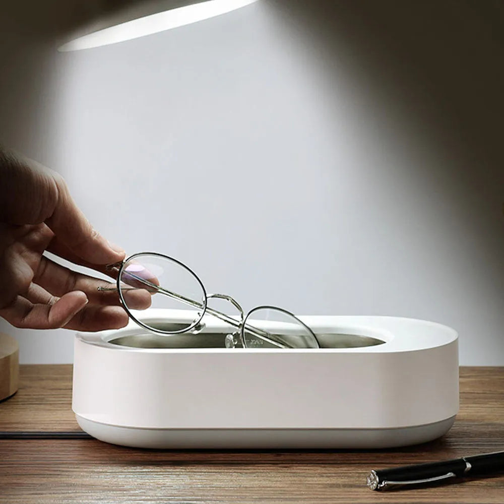 White portable ultrasonic cleaner with stainless steel tank and a single control button.