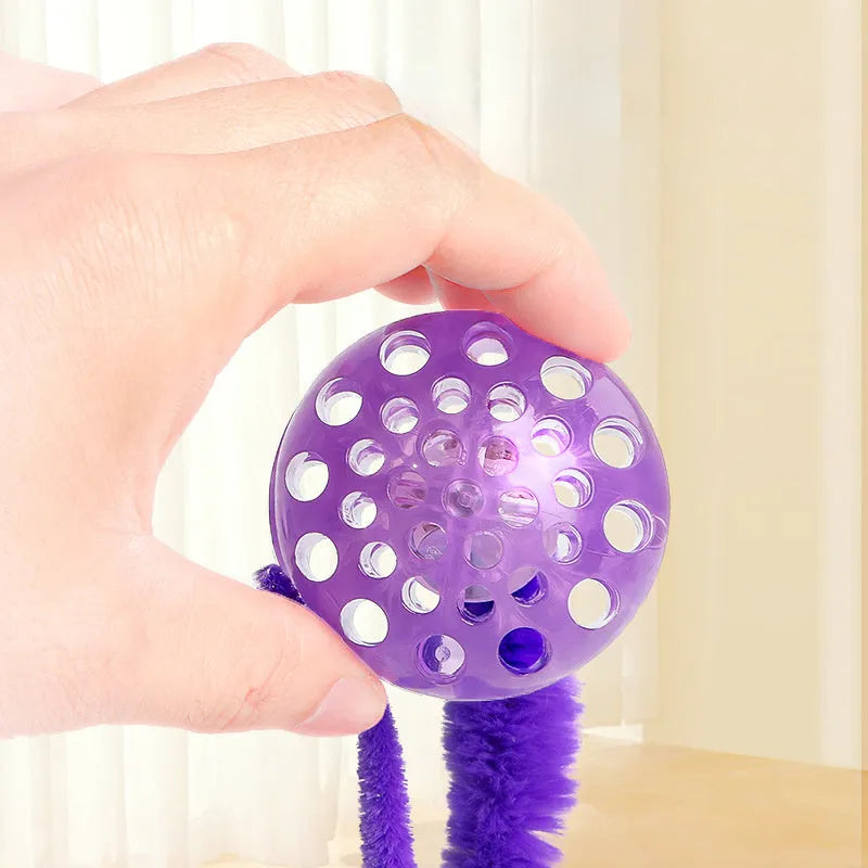 Green bouncy ball cat toy with plush tail on wooden floor